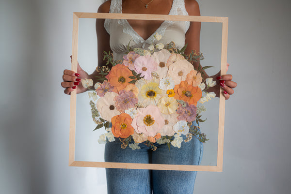 A person holding a wooden frame with colorful pressed flowers