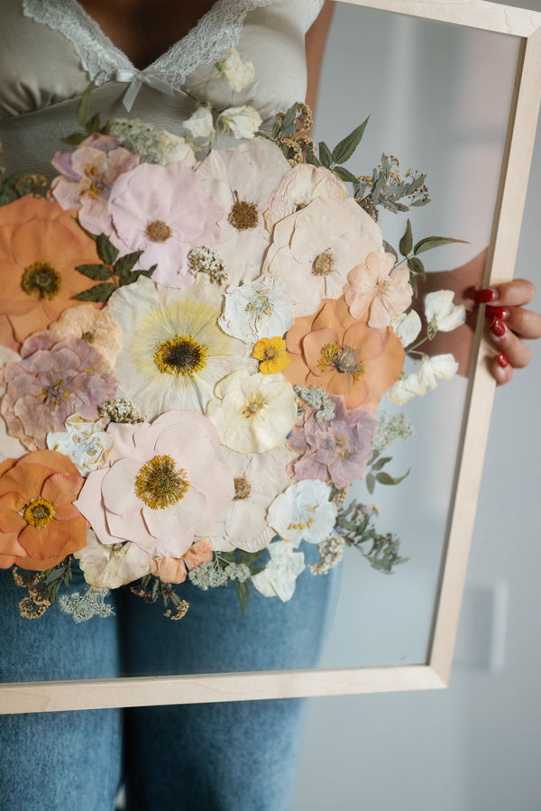 A person holding a framed artwork consisting of a floral pattern