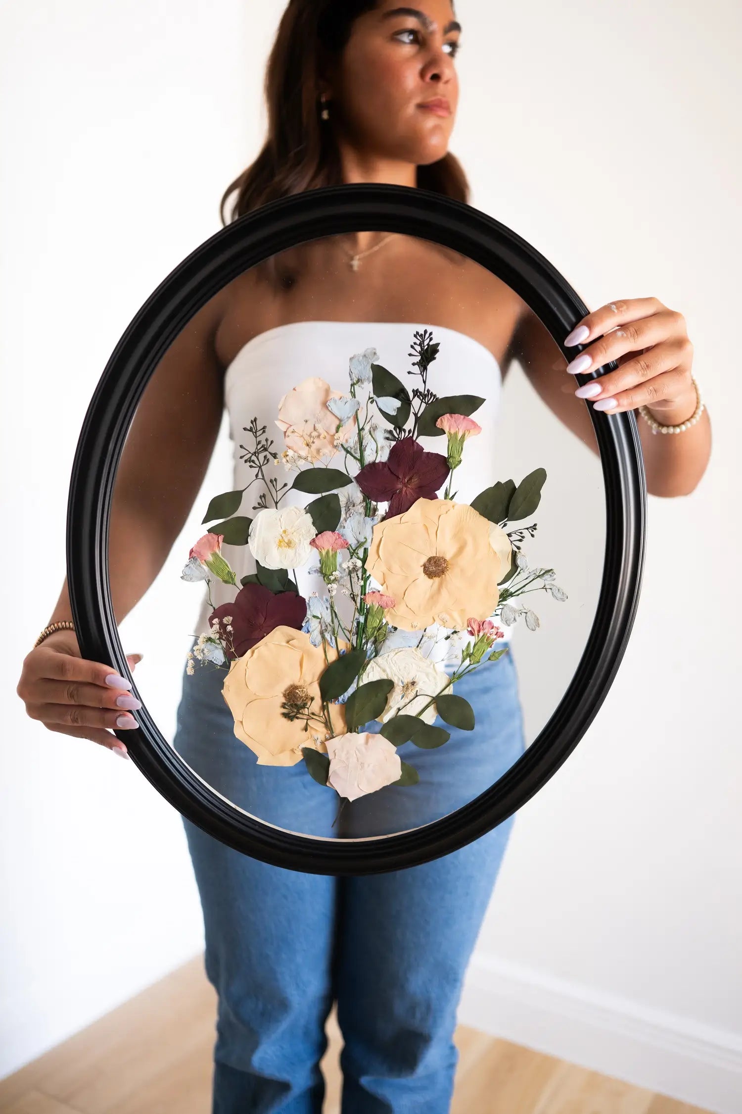 A person holding an 11x14 oval frame with a pressed floral design.