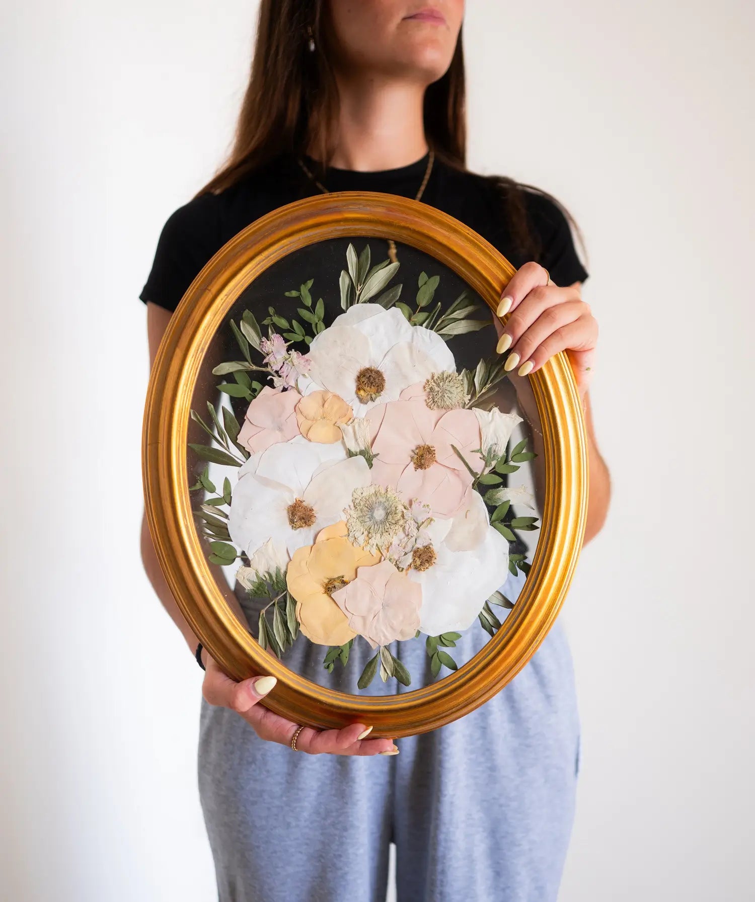 A person holding an 11x14 oval frame with a pressed floral design.