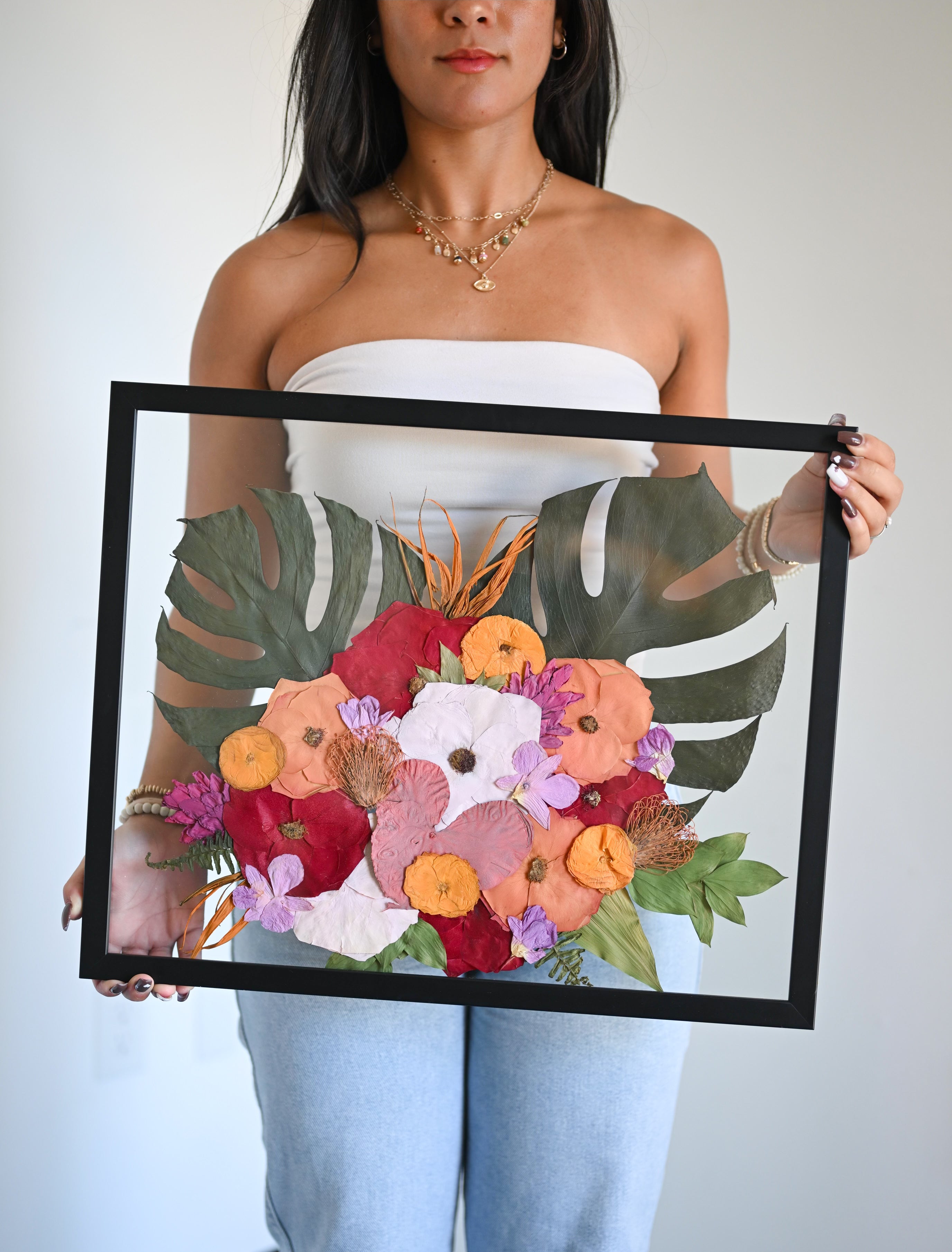 A person holding a wooden frame with preserved floral arrangements inside