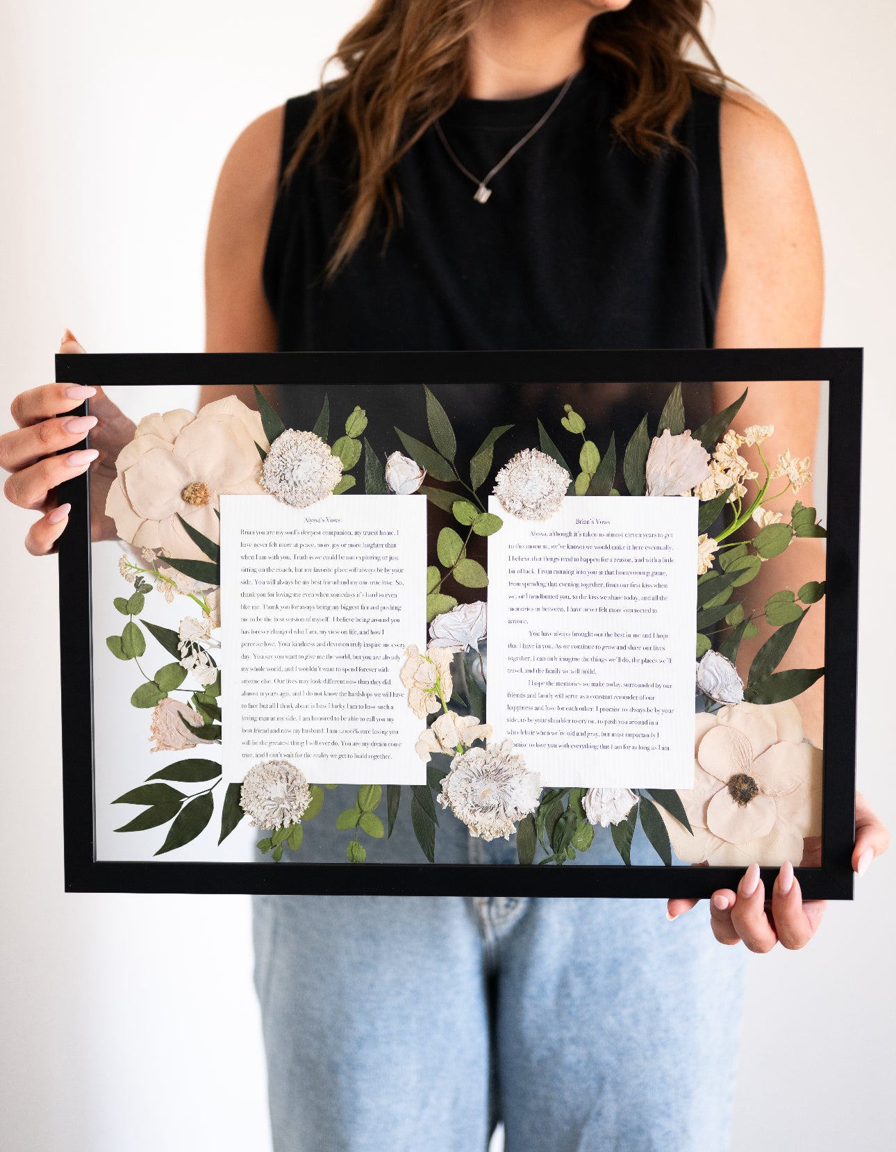 Person holding a framed print with floral design and text.