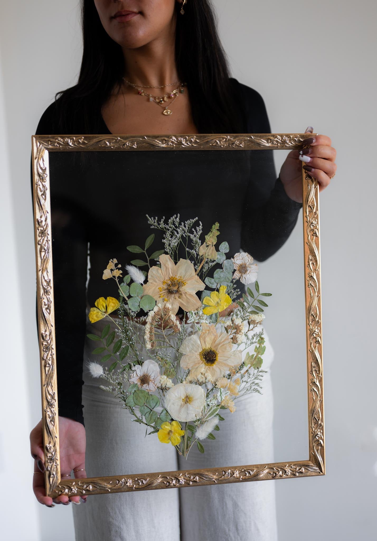 A person holding a floral arrangement in a gold frame