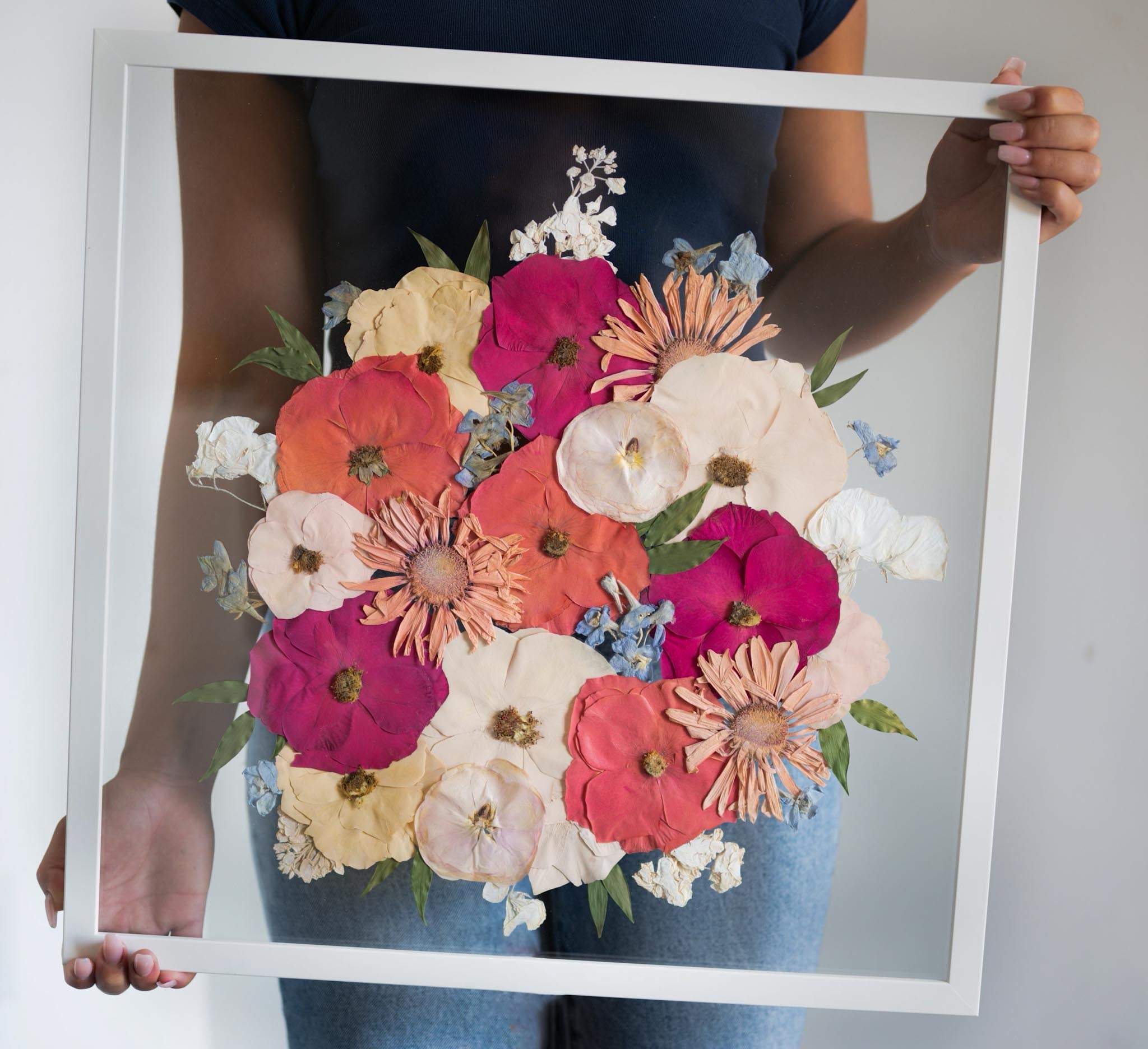 A person holding a frame with a floral artwork inside