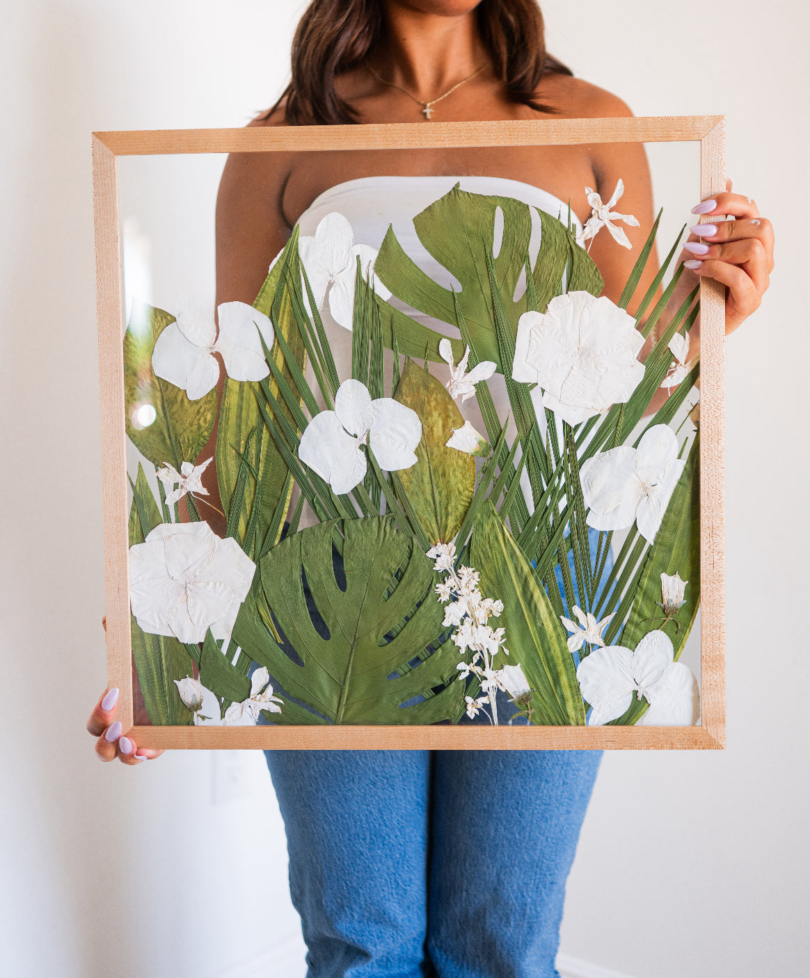 A person holding a wooden frame with a floral artwork