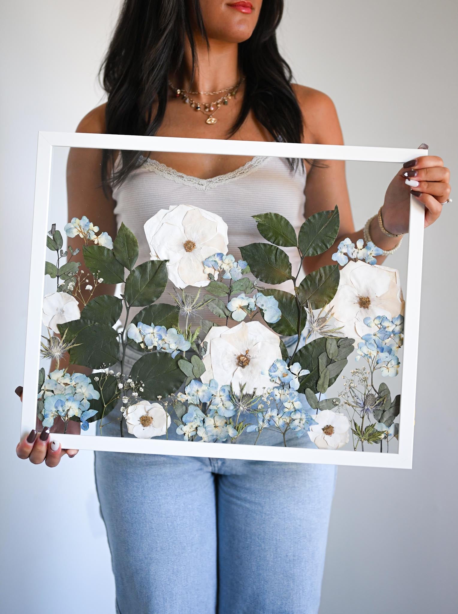 A person holding frame with preserved floral arrangements inside