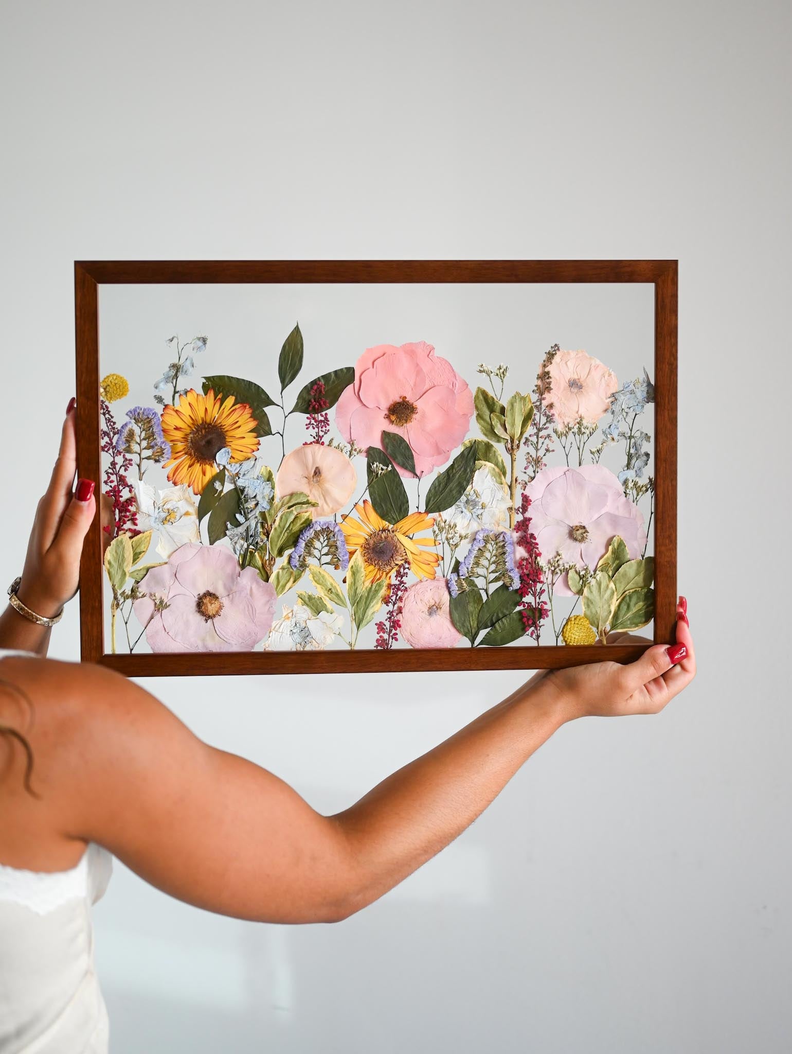 A person holding a wooden frame with a pressed floral arrangement inside it.
