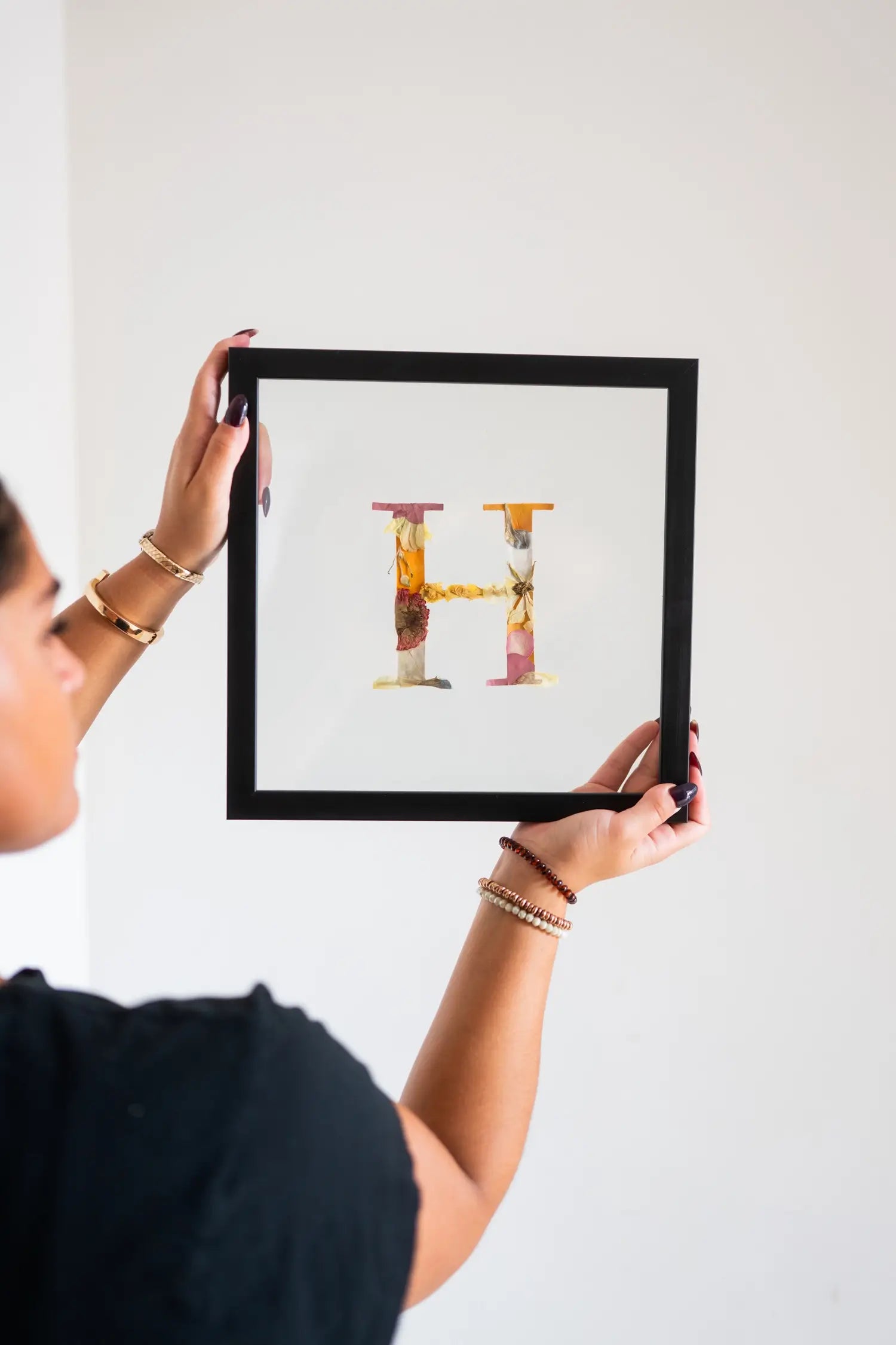 Person holding a framed artwork with a colorful letter 'H'